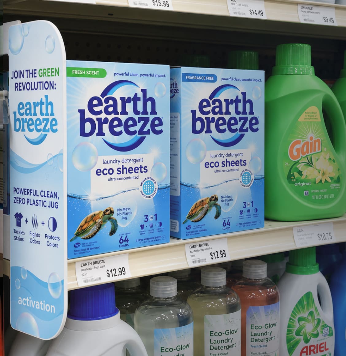 Shelf of laundry detergent products: blue Earth Breeze eco sheets boxes beside a green Gain bottle on the right.