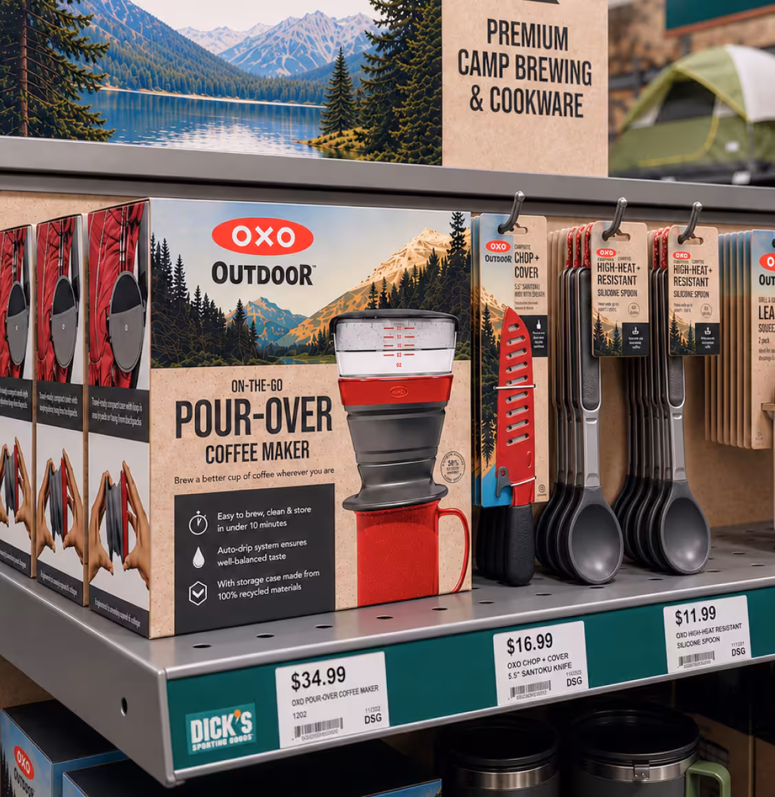 Boxed OXO Outdoor Pour-Over Coffee Maker displayed on a store shelf, with a mountain landscape graphic and camping tools nearby.