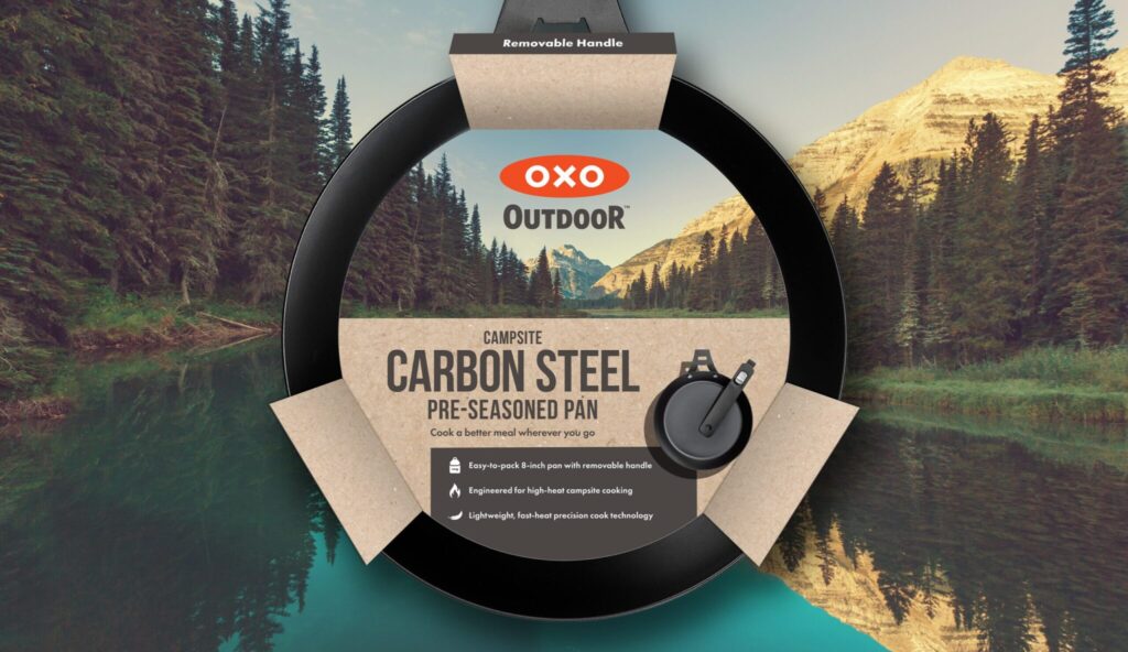 OXO Outdoor carbon steel pre-seasoned pan packaging displayed against a mountainous outdoor backdrop with a removable handle label visible.