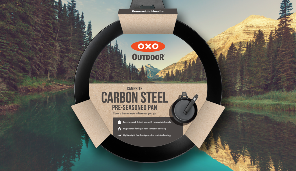 OXO Outdoor carbon steel pre-seasoned pan packaging displayed against a mountainous outdoor backdrop with a removable handle label visible.
